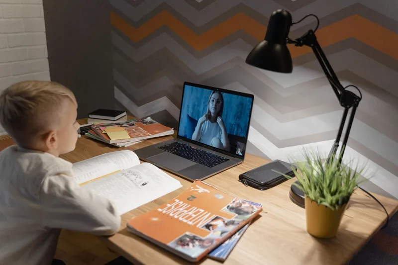 Child completing an online homeschool lesson on a laptop with a teacher on screen