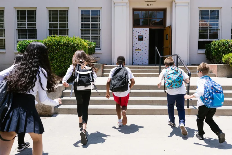 Elementary students with backpacks heading up the steps of their school