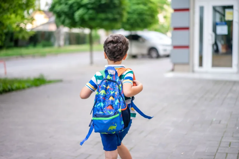 Kindergarten boy with a dinosaur backpack walking into school