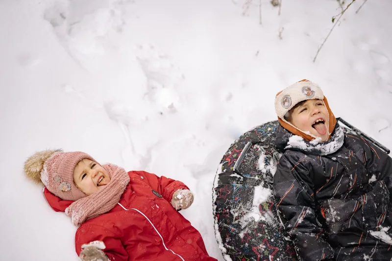 Two kids in winter coats laughing and playing in the snow over holiday break