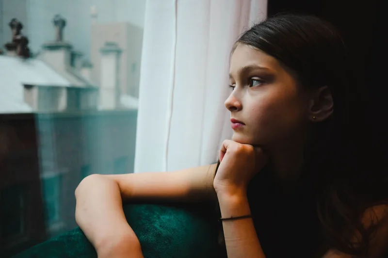 Girl at home alone after school looking out the window