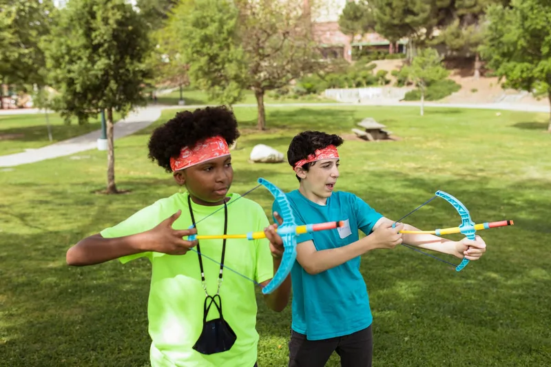 Two campers playing a foam archery game outdoors during a school day off camp